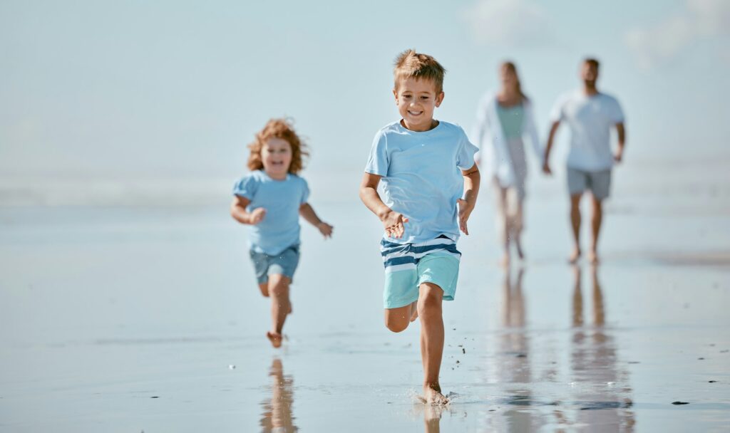 Children, running and beach with a brother and sister together on the sand by the sea or ocean duri